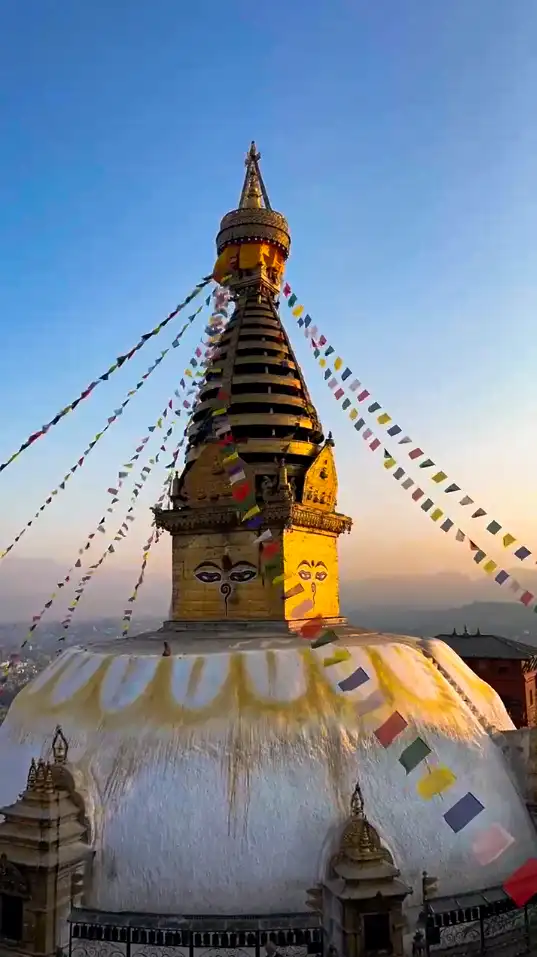 Colorful prayer flags flying at Swayambhunath Temple with white dome and golden spire against blue sky Kathmandu Nepal